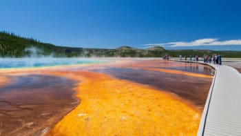 Visitors Stop Along The Wooden Boardwalk To Admire The Vibrant Reds, Greens And Blues Of The Grand Prismatic Spring In Yellowstone National Park